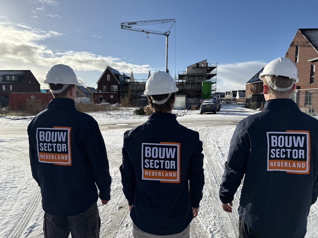 Drie vakmensen van Bouwsector Nederland met witte helm kijken naar een nieuwbouwstraat met een bouwkraan