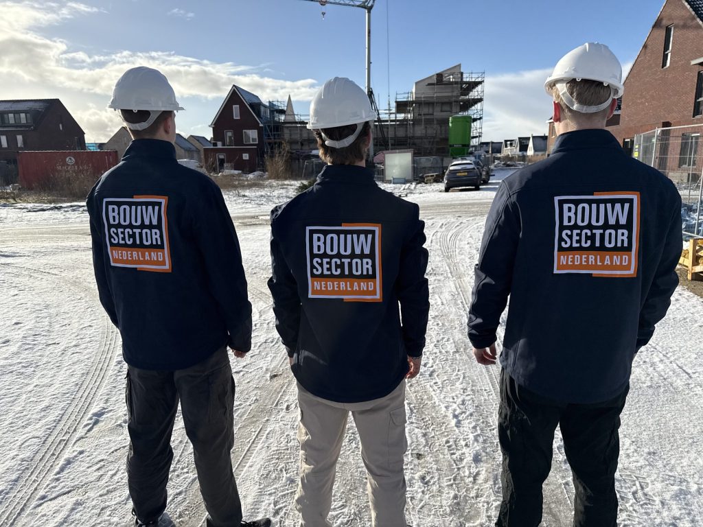 Drie vakmensen met helm en bedrijfsjas van Bouwsector Nederland voor bakstenen woningen in aanbouw