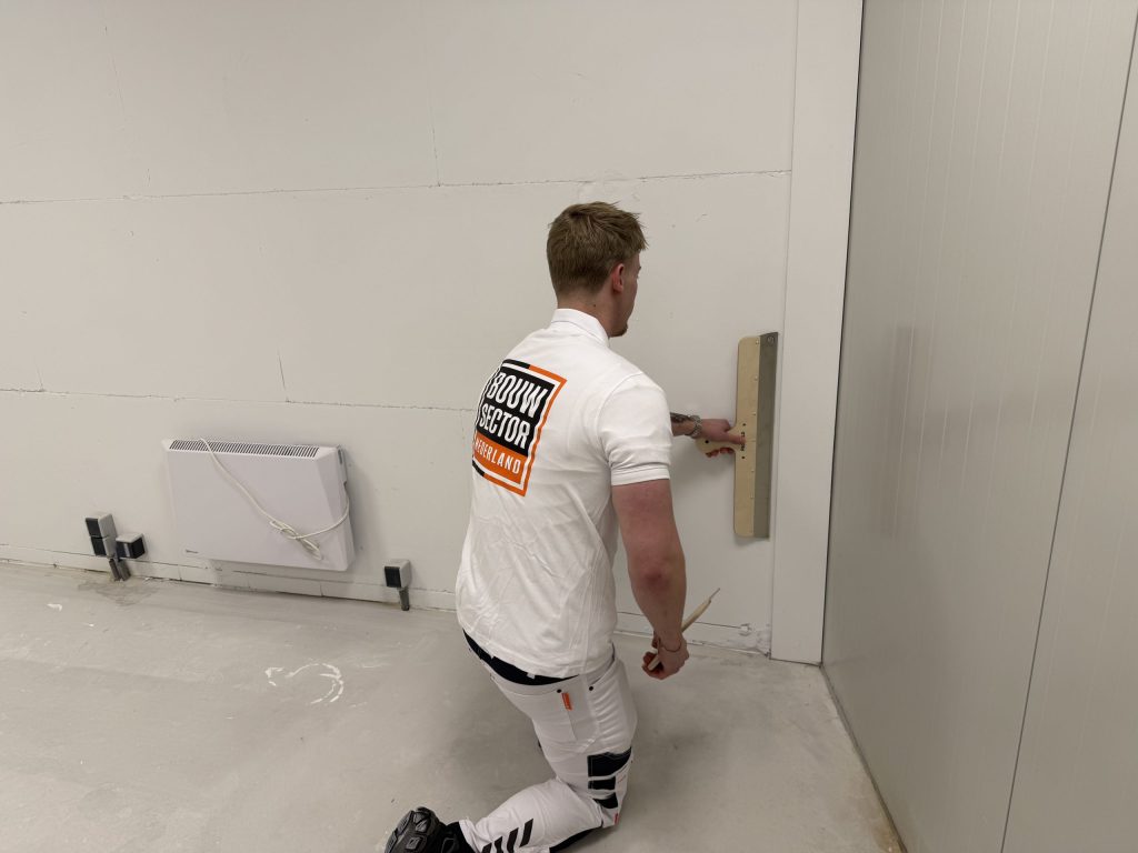 Stukadoor van Bouwsector Nederland zit op een knie en trekt het onderste deel van een wand vlak