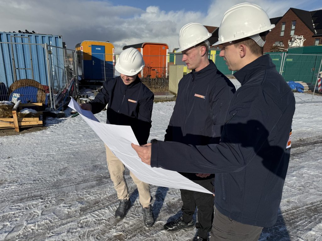 Drie vakmensen van Bouwsector Nederland met helm bekijken samen een bouwtekening op een bouwterrein